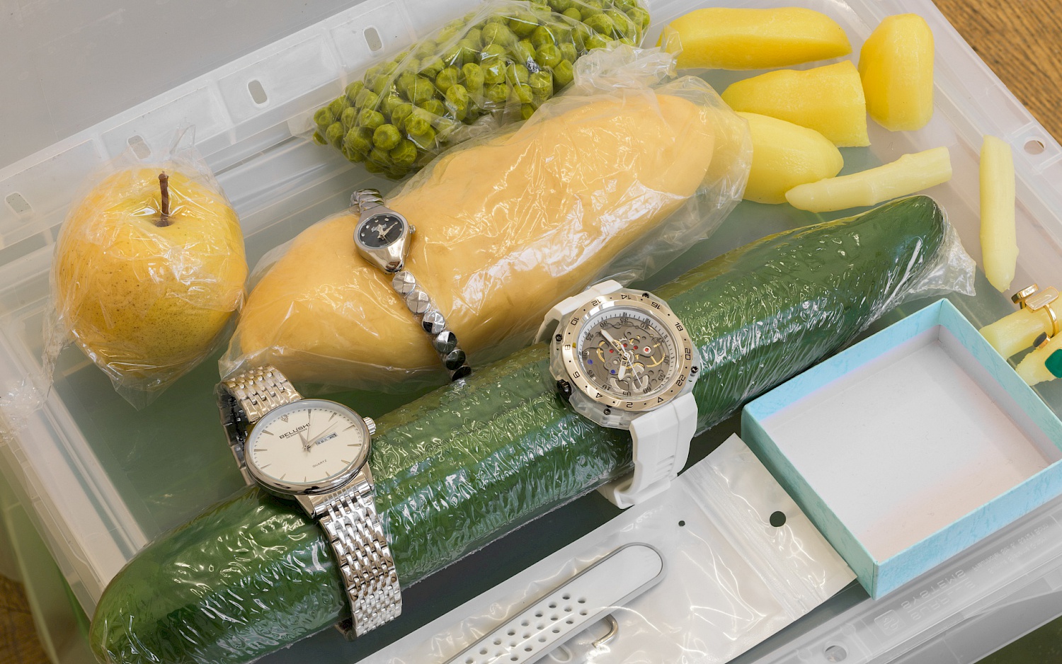 Verschiedenes Obst und Gemüse in Plastikfolie geschweißt und mit verschiedenem Schmuck wie Armbanduhren oder Ringen bestückt.