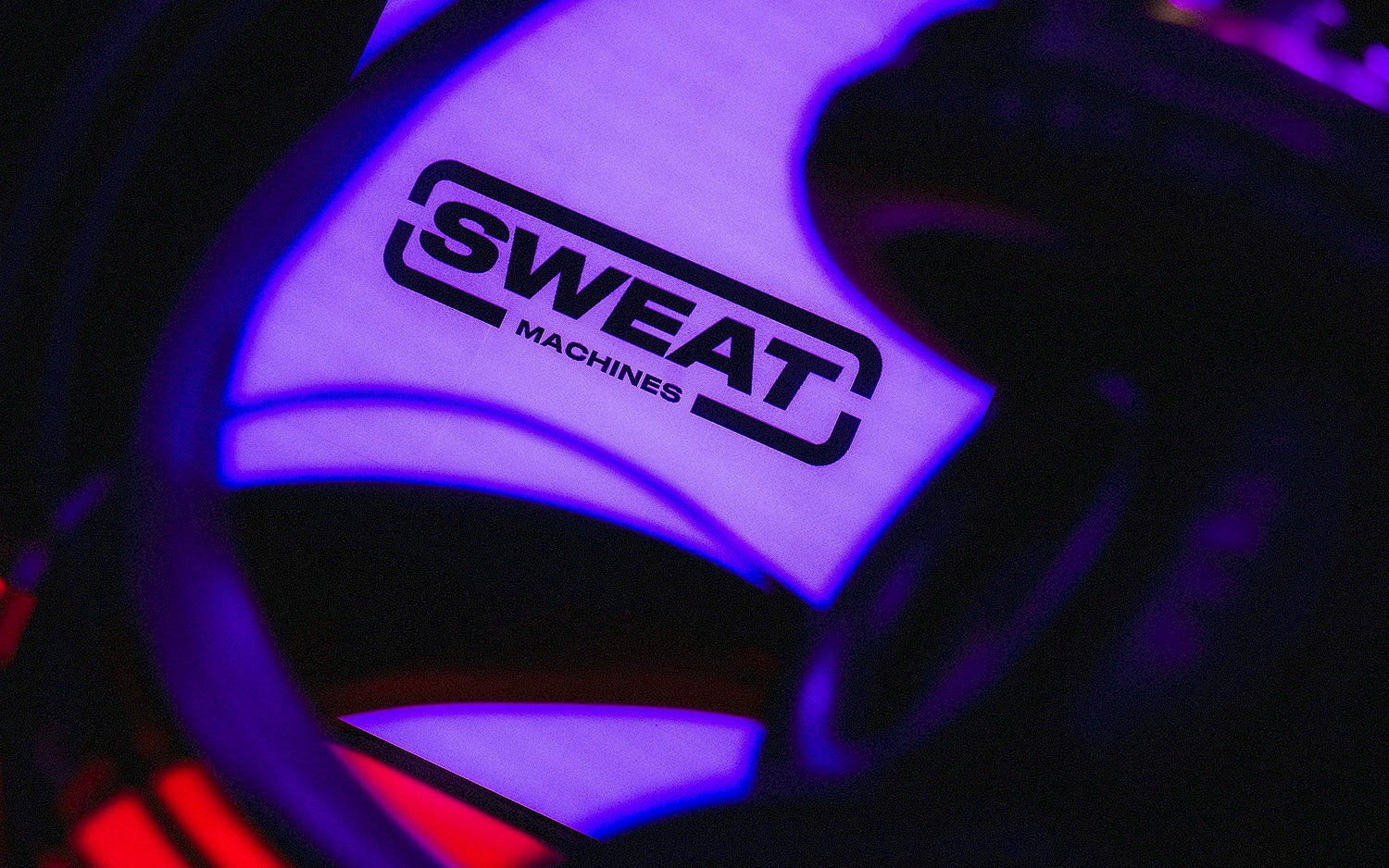 Leuchtendes Logo „SWEAT Machines“ auf violettem Hintergrund, umrahmt von dunklen, verschwommenen Formen im Vordergrund.