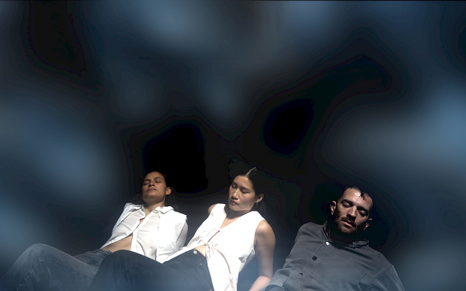 Drei Personen liegen halb aufgestützt nebeneinander und halten die Augen geschlossen.