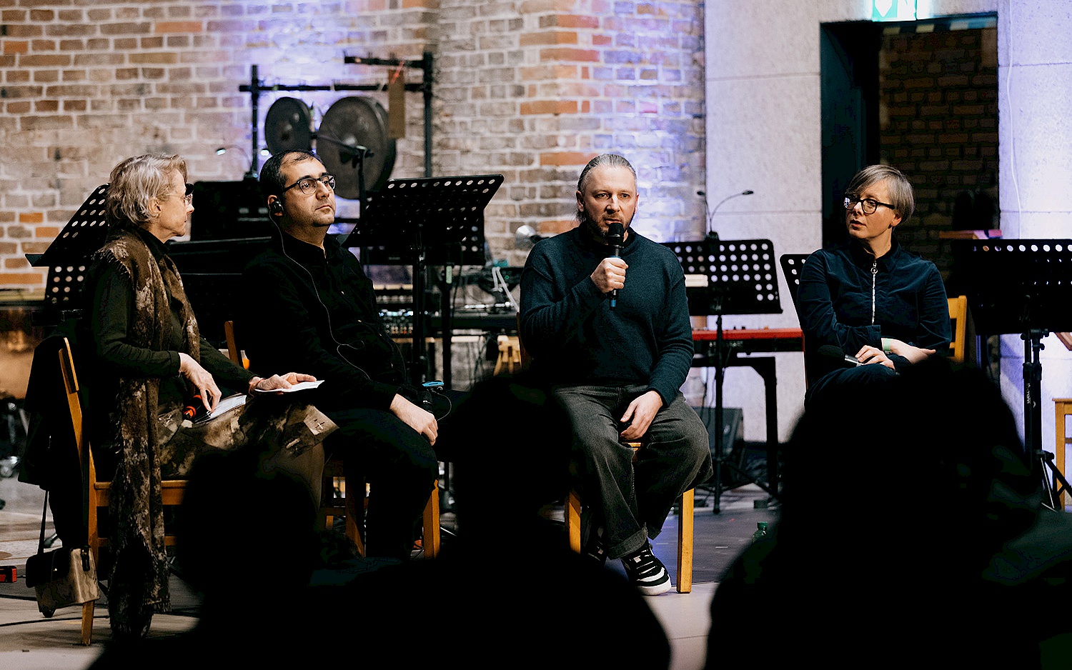 Victoria Nazarova Vier schwarz gekleidete Personen sitzen in einem Panel auf einer Bühne vor Publikum.