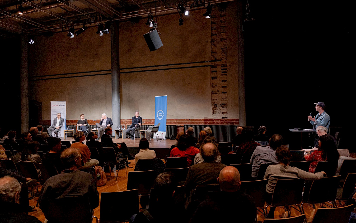 Podiumsdiskussion mit vier Sprecher*innen auf der erleuchteten Bühne