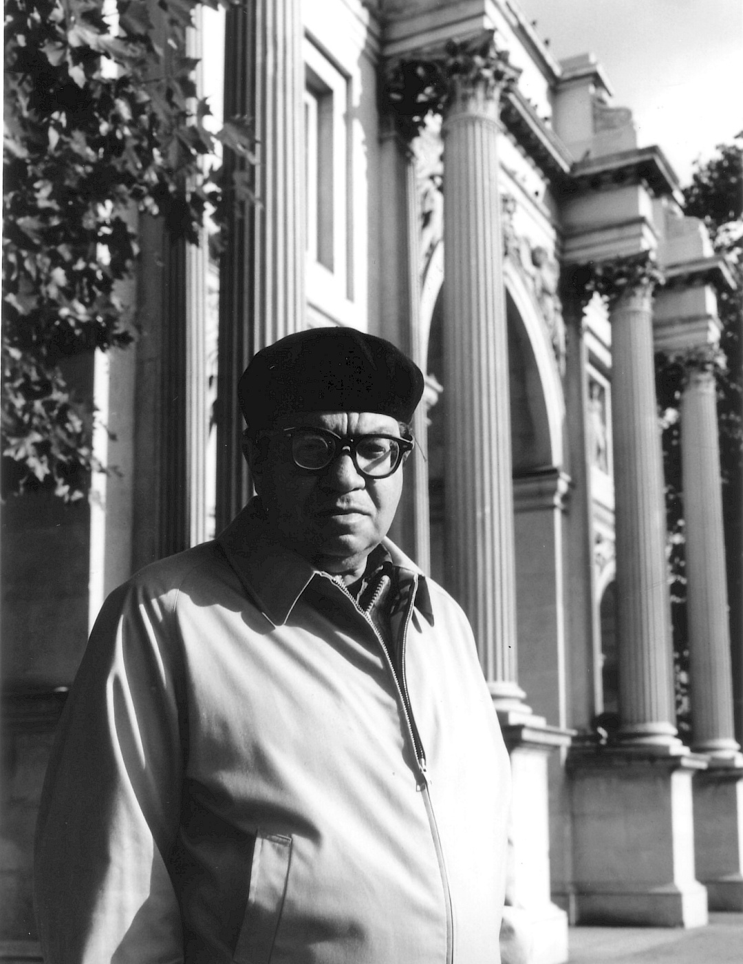 Archiv Universal Edition Schwarz-weiß Portrait von Morton Feldman. Er trägt eine helle Jacke und eine schwarze Mütze. Im Hintergrund ein Gebäude mit Säulen.