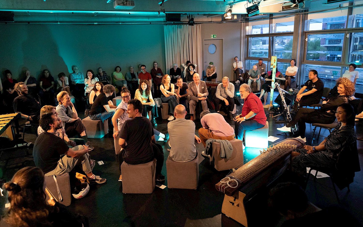 Uta Neumann Besucher*innen und Trickster Orchestra sitzen im Kreis umgeben von Instrumenten im Studio des Radialsystems