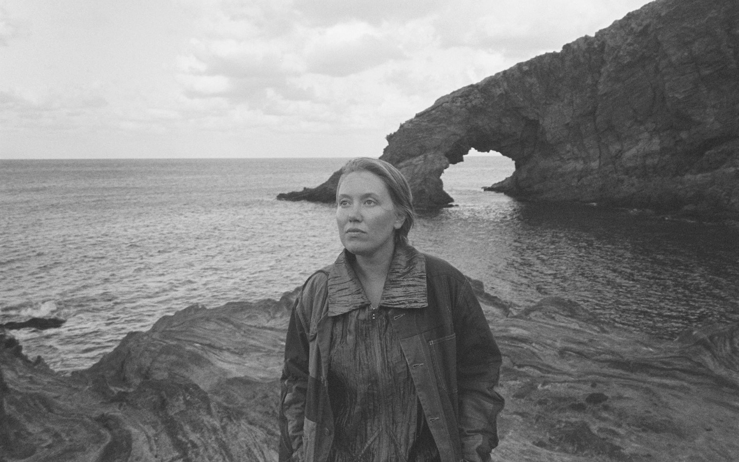 Black-and-white photograph of Ellen Arkbro in front of a cliff by the sea.
