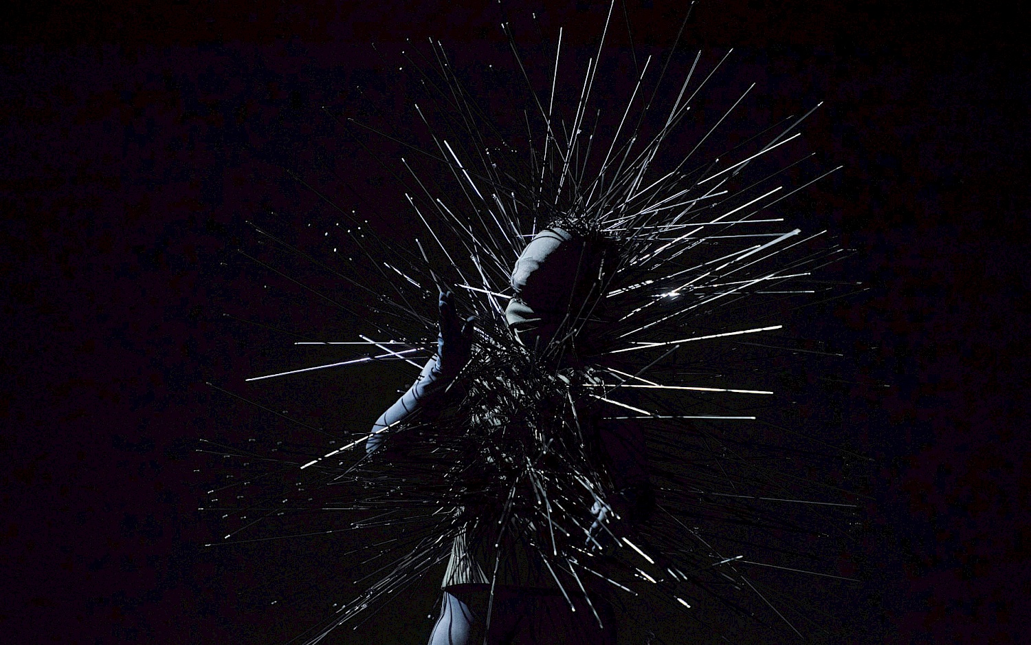 Eine Person mit Kostüm bestehend aus vielen langen Metallstacheln auf einer dunklen Bühne.