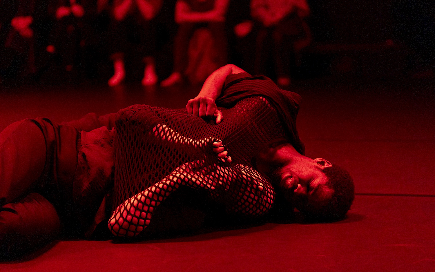 Zwei Performer*innen, die am Boden liegen, die Lichtstimmung ist rot