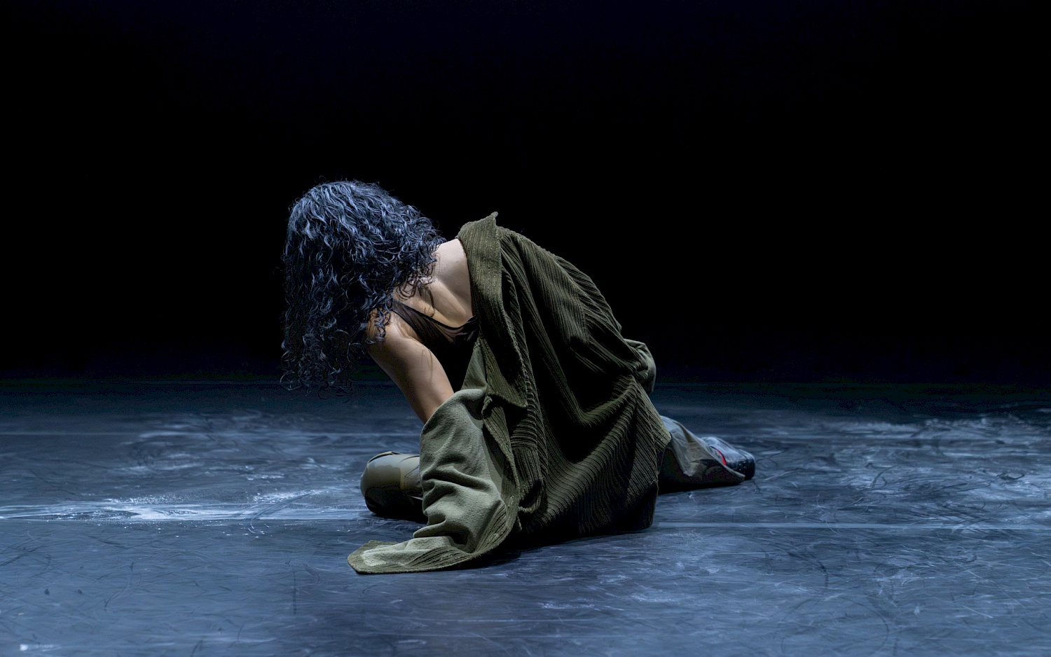 A person with black curly hair is sitting with their back to the viewer. Their upper body is leaning slightly to the left.