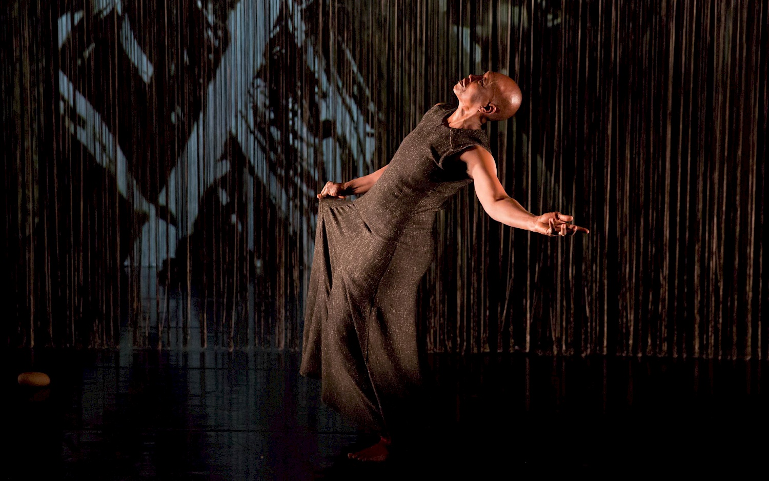 A person in a sleeveless dark dress on a dark stage.