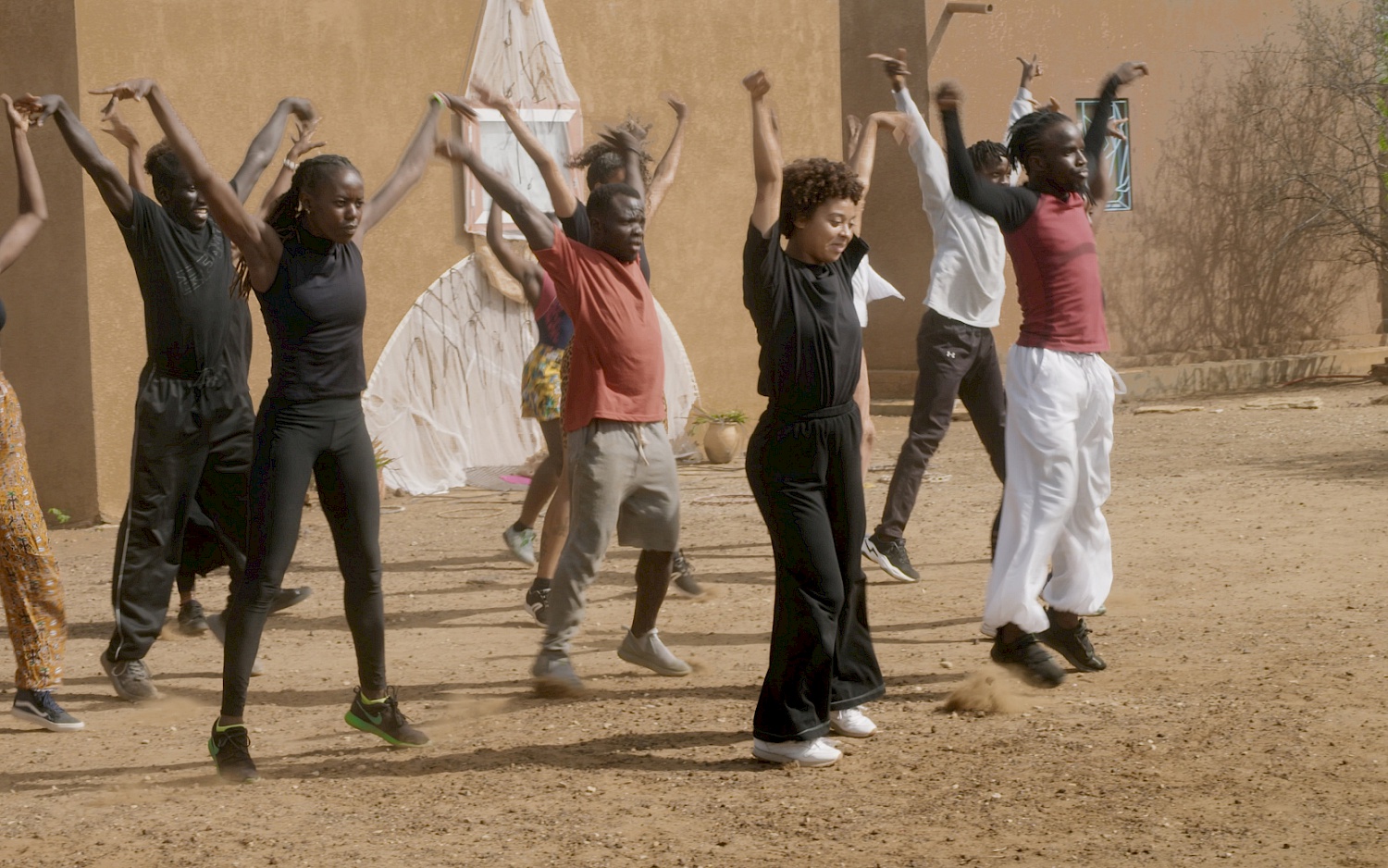 CALA FILM Film still: A group of dancers on dusty sandy ground.
