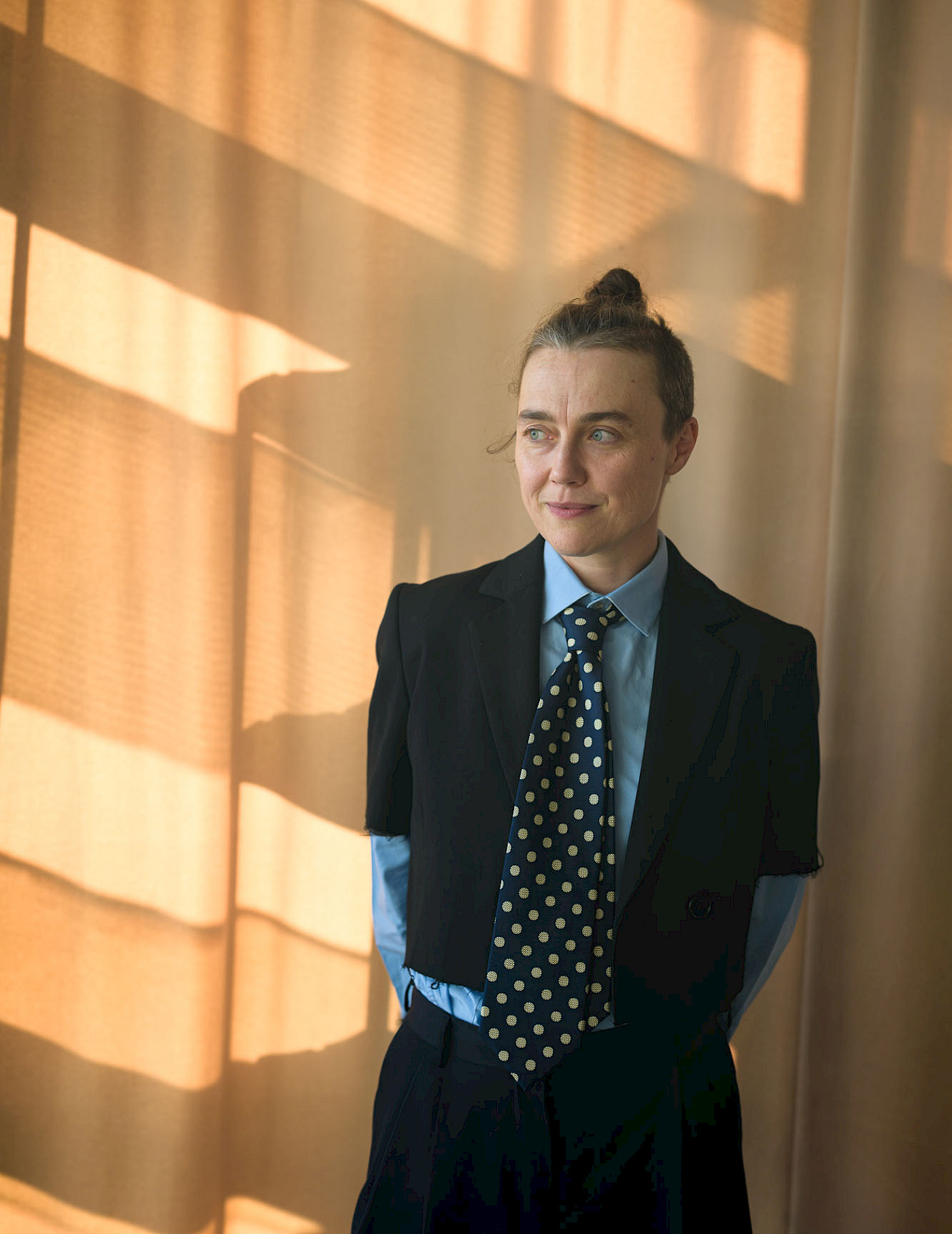 Agata Siniarska in schwarzem Blazer, blauem Hemd und gepunkteter Krawatte vor einem gelben Vorhang.