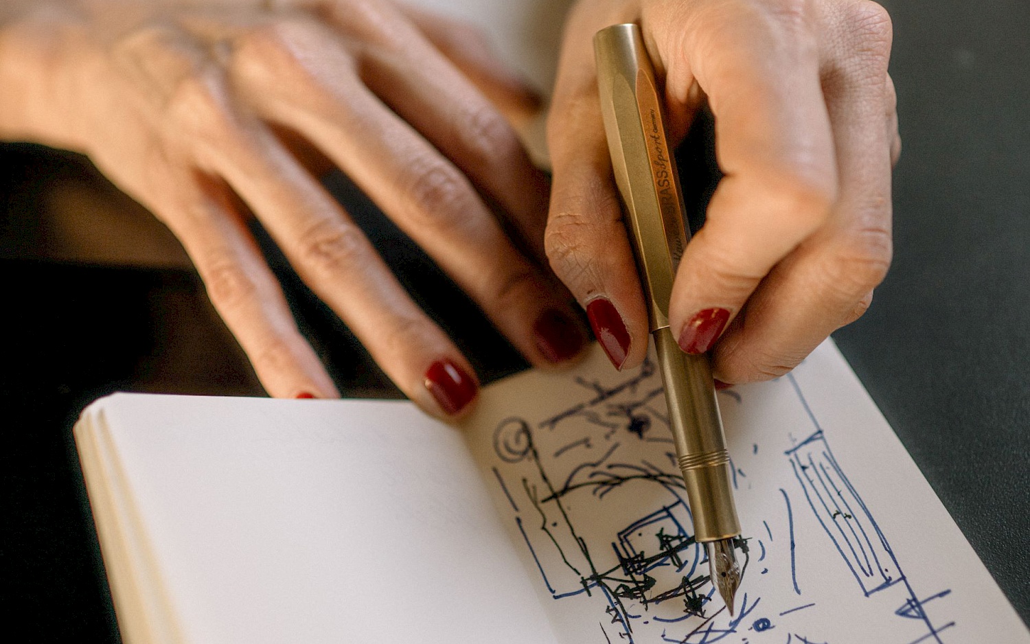 The hands are holding a sketchbook. The left hand is holding a pencil. A square has been drawn in the sketchbook, containing lines, circles and other shapes.