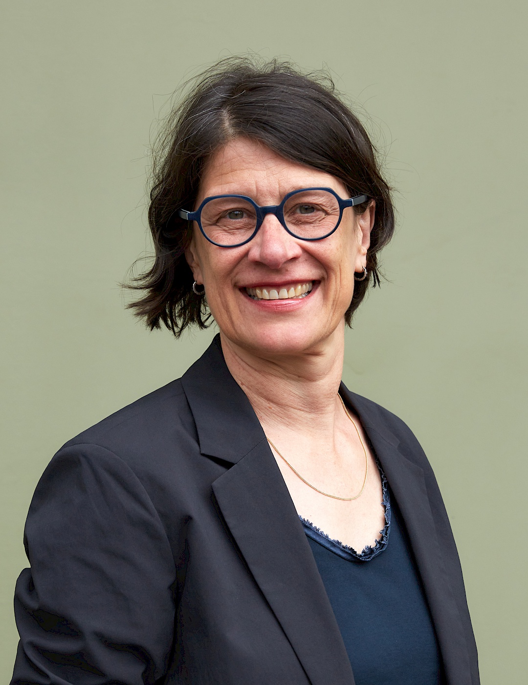 Portrait Hannah Kruse in a black blazer in front of a light green background.