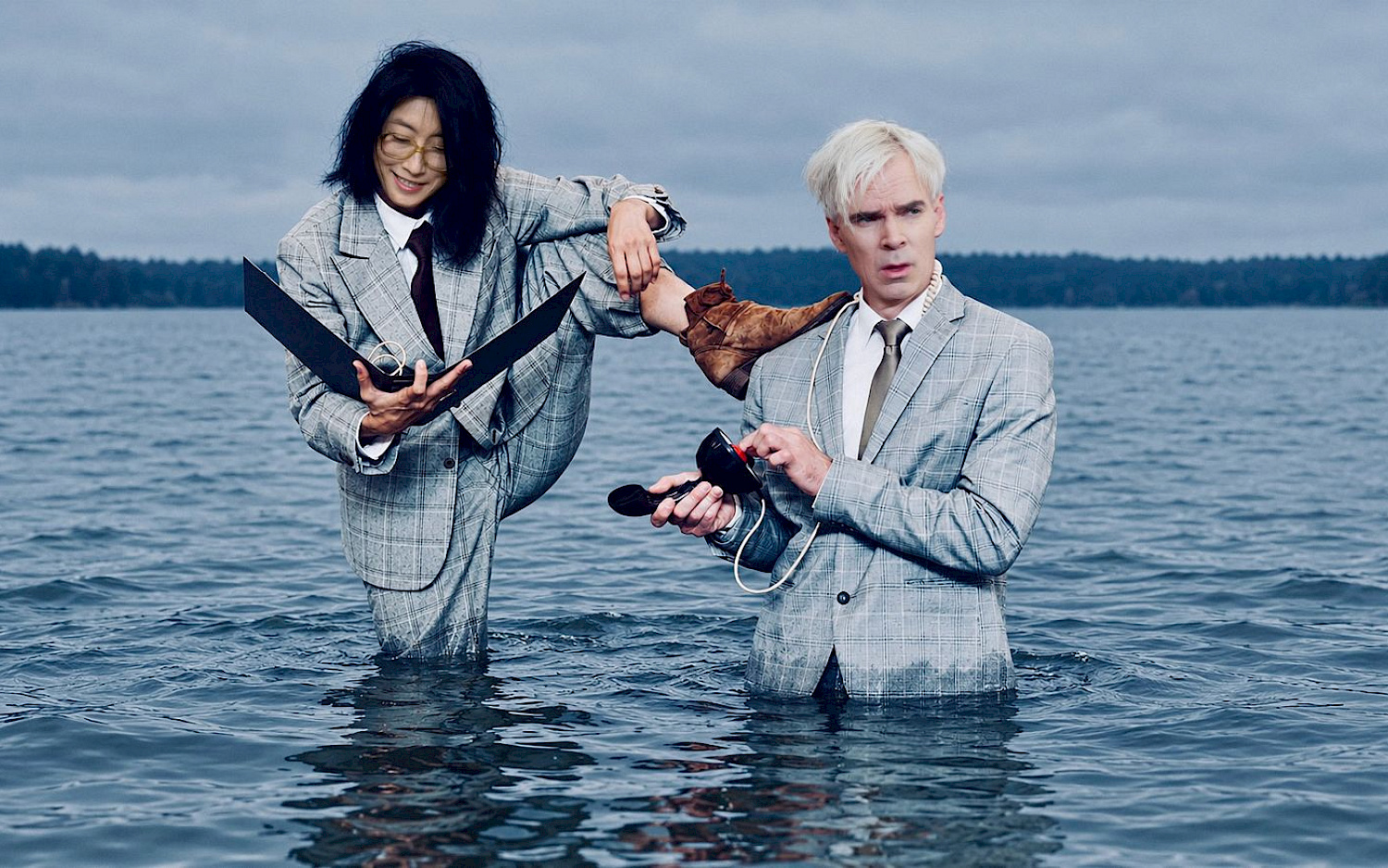 Dieter Hartwig / KI-Bearbeitung NatN Zwei Personen in grauen Anzügen stehen bis zur Hüfte im Wasser. Eine Person hat den Fuß auf die Schulter der anderen gestützt.