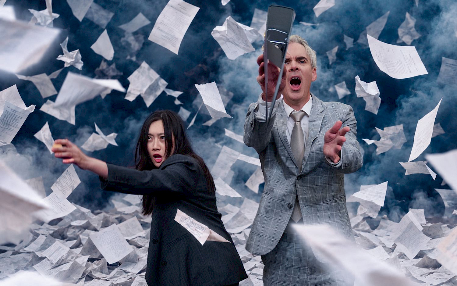 Dieter Hartwig / KI-Bearbeitung NatN Two people in business suits stand beneath a stormy sky, reaching for documents that are swirling wildly through the air.