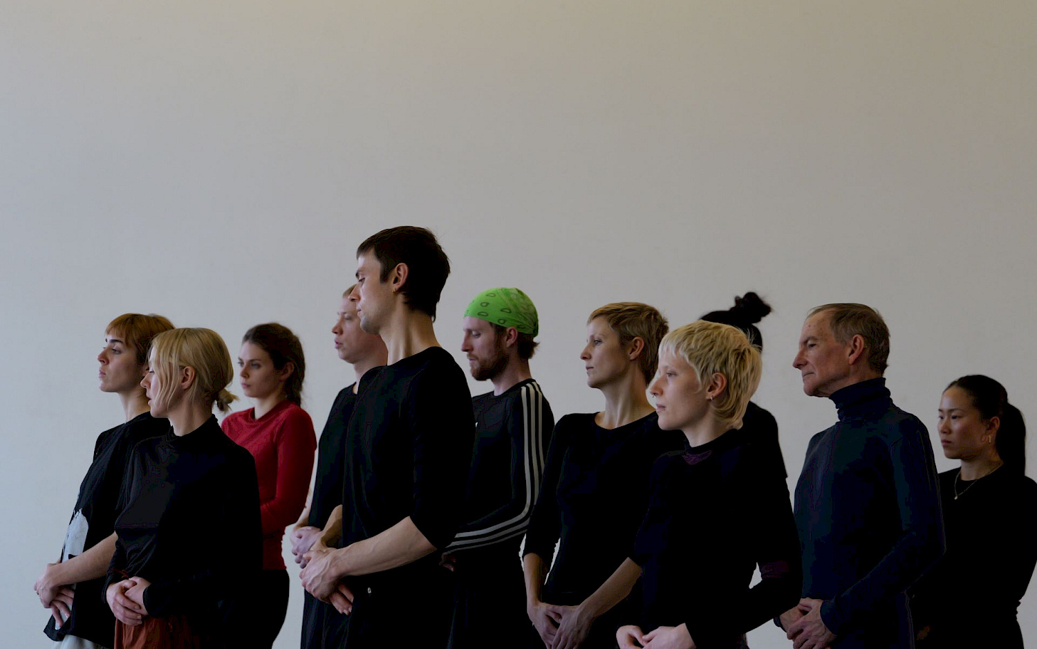 A group of dancers with their hands folded are looking out of the picture from the side.