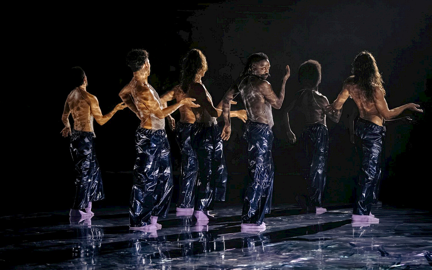 Blandine Soulage Eight dancers in chainmails on a dark stage.