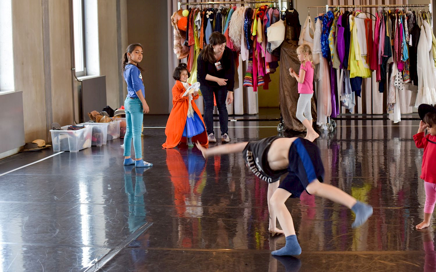 Giacomo Cosua A child is doing a cartwheel. In the background, two children are standing in front of a costume wardrobe.