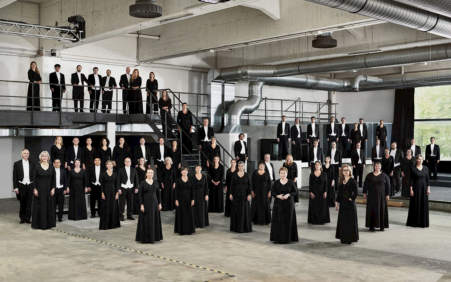 Die Sänger vom Rundfunkchor Berlin stehen in schwarz gekleidet verteilt in einer Industriehalle.