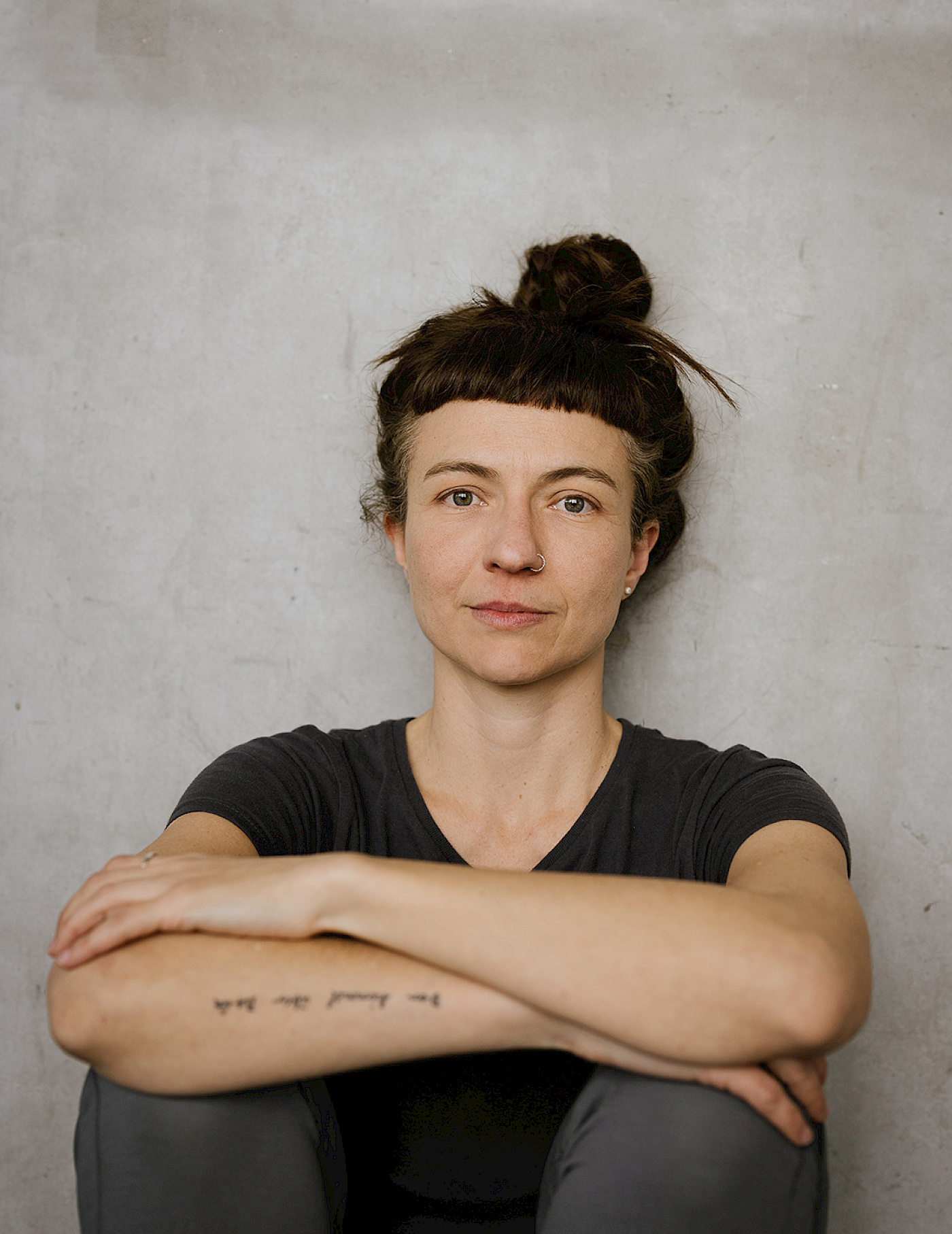 Portrait of Elisabete Finger: She sits leaning against a wall, her arms resting on her knees and smiles into the camera.