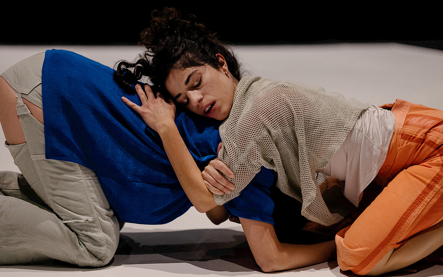 Two dancers embrace each other, while kneeling on the floor.