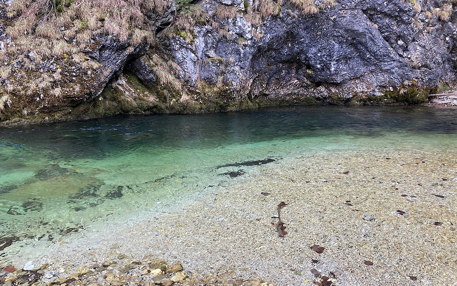 Ein Flussufer mit Kieselstrand auf der einen und steiler Steinklippe auf der anderen Seite.