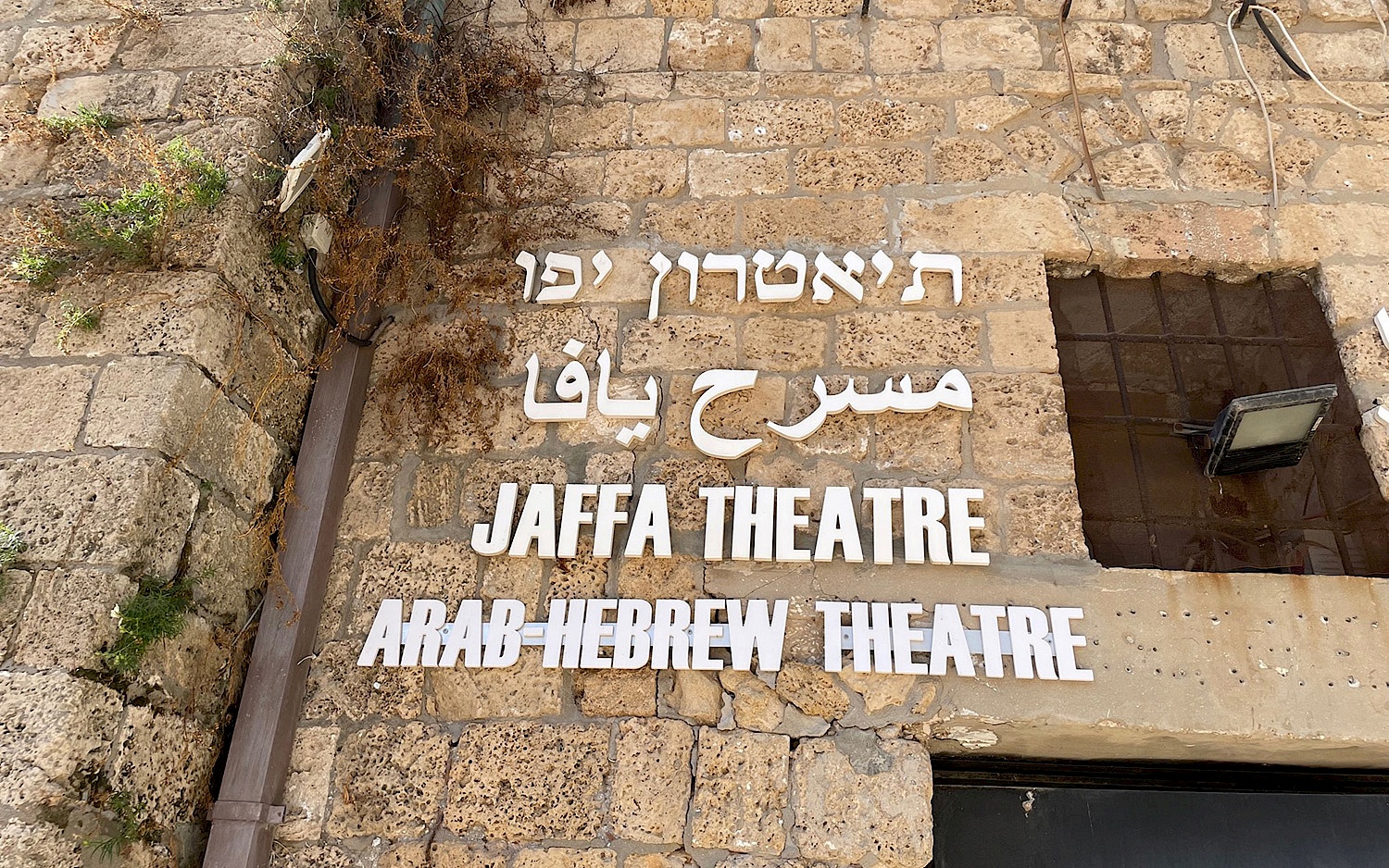 Fassade des Jaffa Theatre, auf der der Name des Theaters in hebräischen, arabischen und römischen Schriftzeichen geschrieben steht.