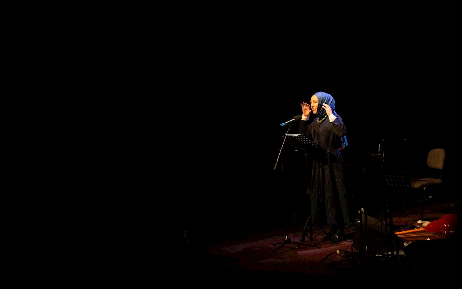 Ein hauptsächlich schwarzes Bild, mit Fokus auf Kübra Gümüşay, die auf der Bühne einen Essay performt.