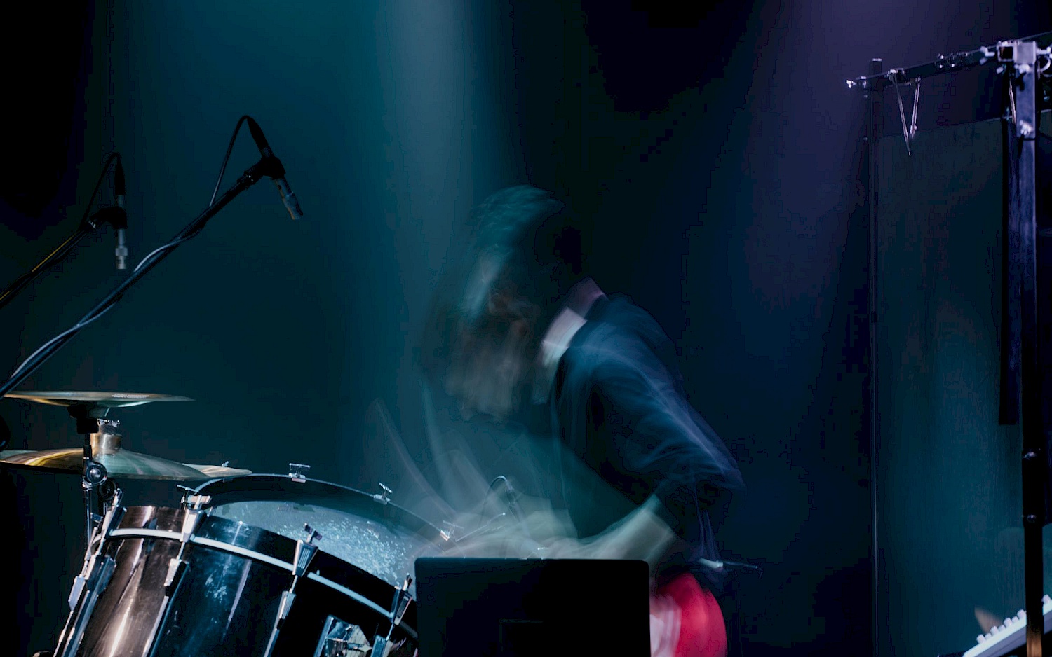 Der Schalgzeuger Aleksander Wnuk beim Konzert seitlich und verschwommen in der Bewegung vor blau-schwarzem Hintergrund.