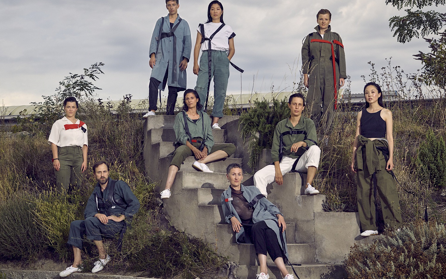 Ensemble Kaleidoskop ist um eine Treppe herum sitzend und stehend angeordnet. Drei Personen sitzen auf der kurzen Betontreppe umgeben von einem Grashang.